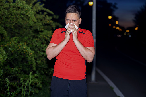 A midnight jogger perseveres through allergy symptoms, clutching tissue paper tightly while maintaining focus on the path ahead, embodying the spirit of endurance and determination
