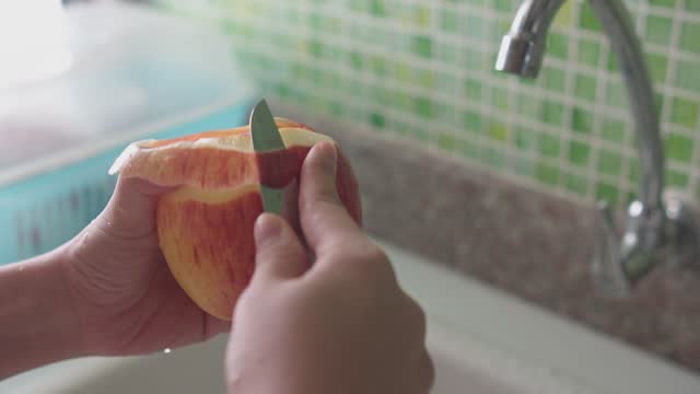 Peeling a Fresh Red Apple in the Kitchen Sink, Healthy Eating and Food Preparation concept.