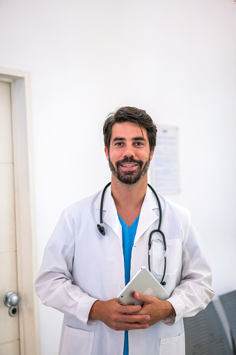 Professional male doctor in a white coat at the clinic, holding a digital tablet, symbolizing healthcare innovations.