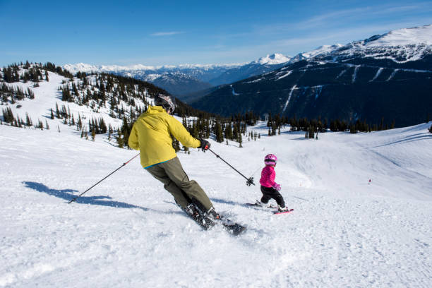 Father and daughter ski down slope at ski resort