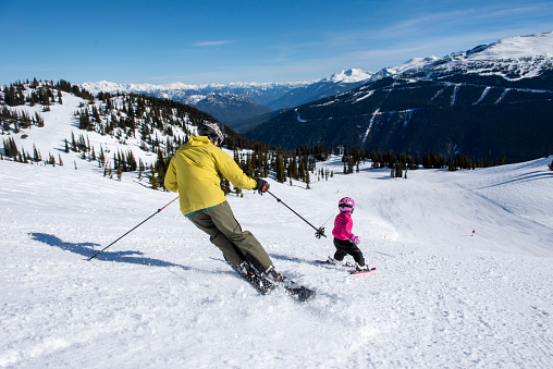 Father and daughter ski down slope at Canadian ski resort on a sunny winter day