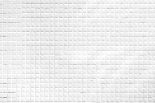 A background of small white square tiles with soft shadows of palm leaves shining on it.