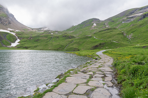 View of the Bachsee surrounded with Swiss mountains during a cloudy summer day. paved walking path.Alpine lake in Switzerland near Grindelwald. Beautiful alpine Swiss landscape. Tourist must-see spot.