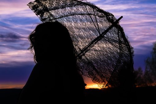 a woman with a lace umbrella in the sunset