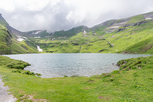 View of the Bachsee surrounded with Swiss mountains during a cloudy summer day. Alpine lake in Switzerland near Grindelwald. Beautiful alpine Swiss landscape. Tourist must-see spot.