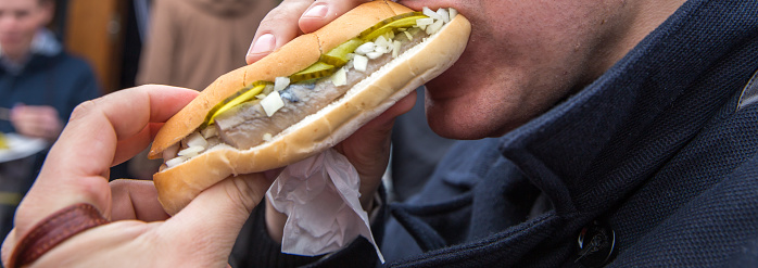 Man eating on a street Seafood burgers with herring, onion and pickle