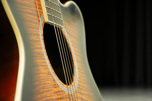 On an empty stage, a lone guitar awaits its moment in the spotlight. The close-up shot captures every detail of its polished body, from the intricate inlays on the fretboard to the subtle curve of its soundhole. Bathed in the soft glow of stage lights, the guitar emanates a sense of anticipation and excitement, as if eager to lend its voice to the music that will soon fill the air.
