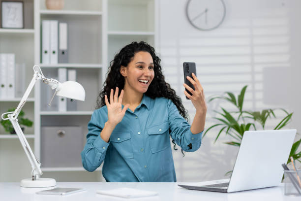 istock Smiling woman waving during a video call at her desk 2148402559