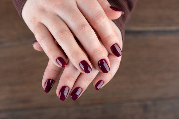 istock Female hands with blackberry-colored manicure over wooden background. 2148402949