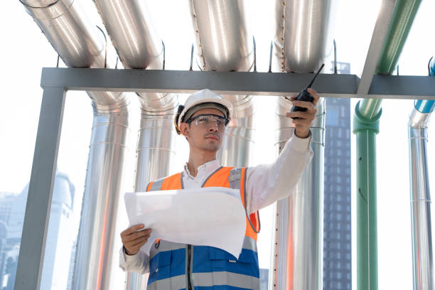 istock Asia male engineer in protective workwear is performing a conducts system check and use walkie talkie with paper work at rooftop building 2148404370