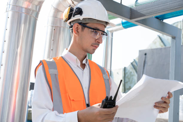 istock Asia male engineer in protective workwear is performing a conducts system check and use walkie talkie with paper work at rooftop building 2148404372