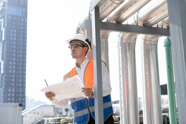 istock Asia male engineer in protective workwear is performing a conducts system check and use walkie talkie with paper work at rooftop building 2148404381