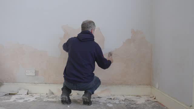 Elderly gentleman working on apartment renovation, wall paint scrapping