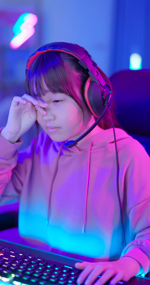 closeup asian young female teenager gamer feel uncomfortable rubbing eyes while play online internet cyber sport game at home