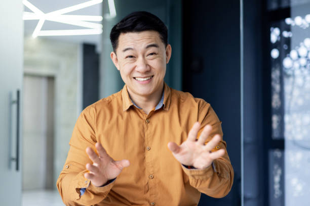 istock Joyful successful businessman watching in web camera, smiling man talking with colleagues remotely using video call on laptop, asian man at workplace inside office 2148409658
