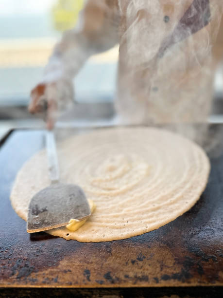 Stock photo showing close-up view of dosa pancake being cooked on hot stove top for breakfast.