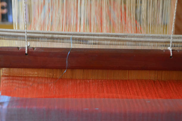 Close-up view of a traditional weaving loom with red and white cotton yarn threads that forms a weft of the fabric in the traditional technique of Laos called Ghot