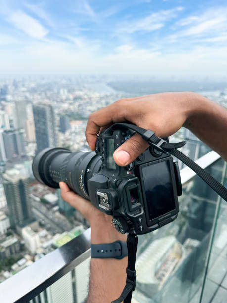 istock Image unrecognisable person on observation deck, taking cityscape photographs with digital SLR camera, zoom lens balanced on glass safety barrier railing, skyscraper skyline, downtown, city centre Bangkok, Thailand, sunny blue sky, fluffy clouds 2148411148