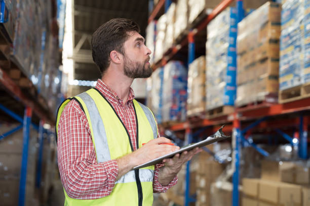 istock Male warehouse worker holding clipboard during working in storage warehouse. Warehouse worker inspecting quality of products on shelf pallet and checking stock inventory 2148411824