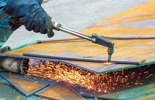 Close up of welder hand is cutting iron plate with acetylene gas welding torch machine at outdoor workshop