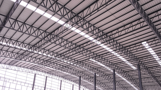 Curve metal roof beam structure with aluminum corrugated steel roof and skylights inside of large industrial warehouse building, low angle and perspective side view
