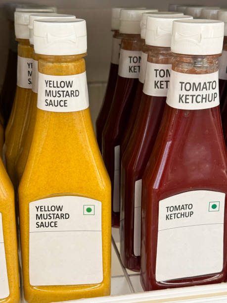 istock Full frame image of retail shelf containing rows of labelled plastic bottles full of condiments, capped bottles of yellow, mustard sauce and red, tomato ketchup, focus on foreground 2148415559