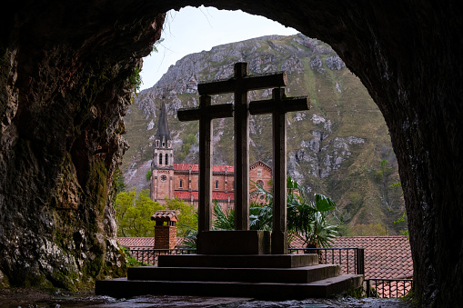 A cross is featured prominently in a cave, with a mountain looming in the background. The rugged terrain adds to the mystique of the scene