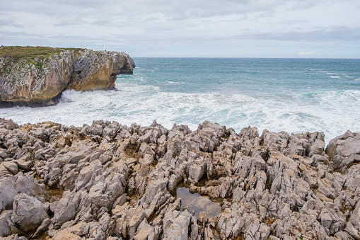 A view of the rugged rocky shore at Los Bufones de Llanes, Asturias, with sharp rocks jutting out into the expansive body of water.
