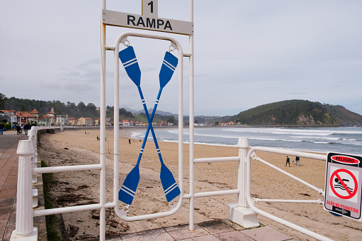 A sign planted in the sand on a beach, with two blue kayaks attached to it. The kayaks are securely fastened and ready for use by beachgoers.