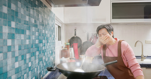asian elderly woman is using wok to cook with much oil smoke in kitchen - one of the causes for lung cancer
