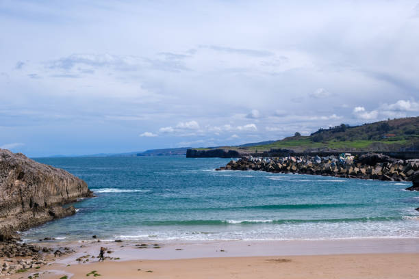 istock A sandy beach stretches alongside the ocean under a cloudy sky, with waves gently rolling onto the shore. In the distance, mountains of Llanes, Asturias, can be seen 2148417038