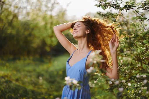 Woman with a beautiful smile with teeth and long hair flying hair in the spring sunset in nature in the park near the flowering trees happiness, natural beauty and hair health. High quality photo