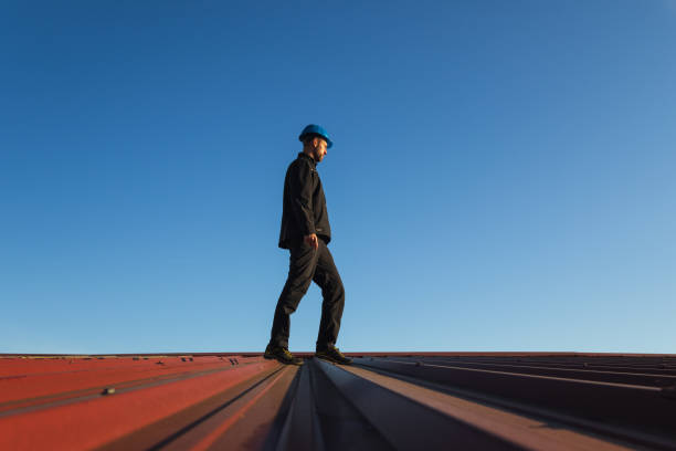 istock Young man worker in helmet standing on roof with blue sky. Roofer work background 2148421255
