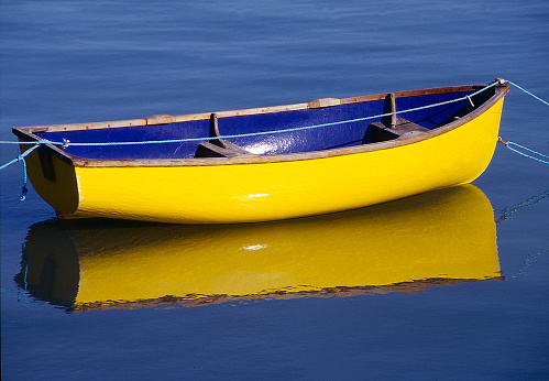 Yellow wooden rowing boat on still water with reflection