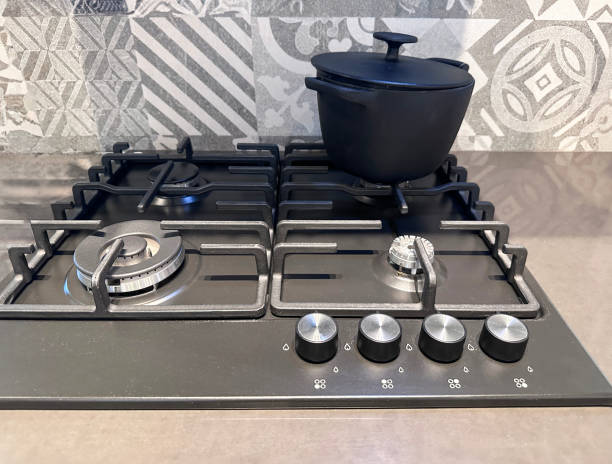 istock Close-up image of modern kitchen 4 burner gas hobs in beige-grey quartz worktop counter, cast iron cooking pot on back burner, grey and white patterned tiled wall, elevated view, focus on foreground 2148424540