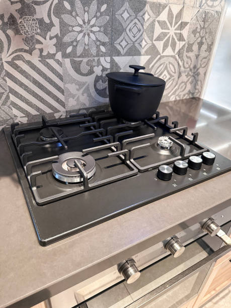 istock Image of modern kitchen 4 burner gas hobs in beige-grey quartz worktop counter, cast iron cooking pot on back burner, grey and white patterned tiled wall, elevated view, focus on foreground 2148424562