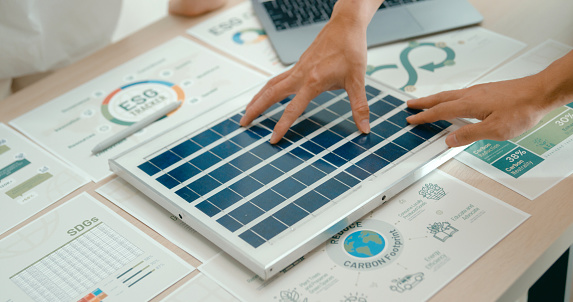 Closeup of diverse team business meeting gathers around laptop in office to discuss sustainable design options involving solar and wind energy. Eco-Friendly Business Team Discussing ESG Goals concept.