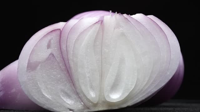 Macrography of sliced red onion against a sleek black background. Comestible.