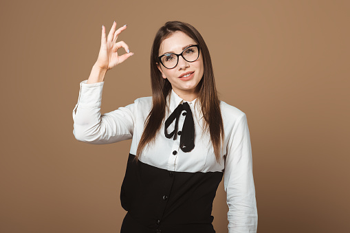 Young Beautiful Brunette in Glasses and White Shirt Gesturing Okay. Positive Image Conveying Approval, Well-being, and Confidence. Ideal for Lifestyle, Fashion, and Positive Expression-themed