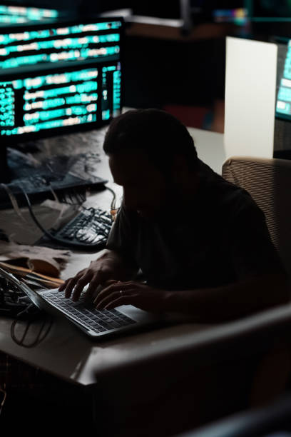 istock Image of unrecognisable man sat in darkness at desk typing on a laptop computer, secret computer hacker programmer, computer coding background, focus on foreground, Internet crime concept 2148429391