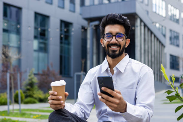 istock Smiling businessman using smartphone while enjoying coffee break outdoors 2148429392