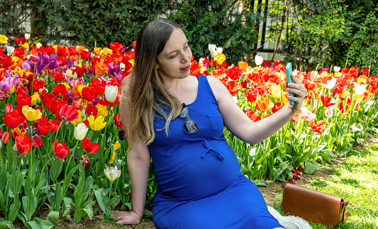 Beautiful pregnant  woman feeling lovely doing selfie and smile in the park