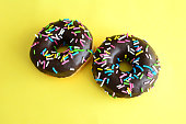 two donuts with sprinkles on a yellow surface