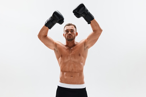 Man athletic bodybuilder poses in boxing gloves with nude torso abs in full-length background, boxing and martial arts. Advertising, sports, active lifestyle, competition, challenge concept. . High quality photo