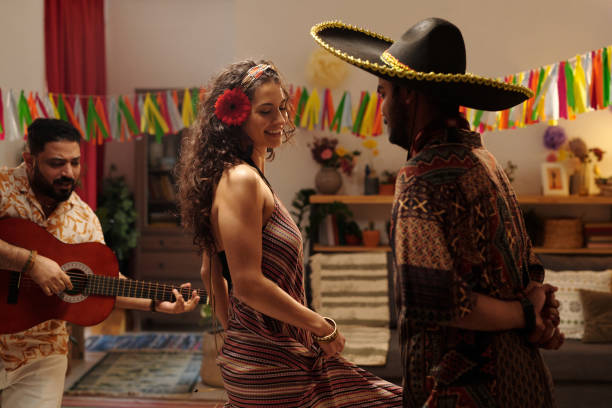 Young cheerful brunette woman dancing in front of Hispanic man wearing sombrero hat while musician playing acoustic guitar at party