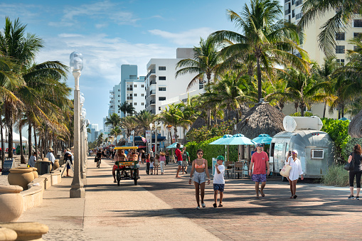 Fort Lauderdale, Florida - April 3, 2023:  People walk by the outdoor restaurants, bars, boutiques and luxury hotels along the palm tree lined beach side boardwalk by the Atlantic Ocean in Ft. Lauderdale Florida