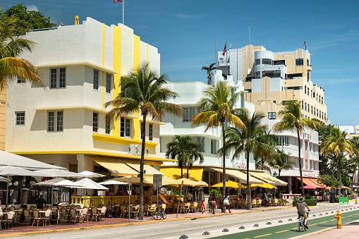 Miami, Florida - April 3, 2023:  People walk and bike along Ocean Drive by the outdoor restaurants, bars, boutiques and luxury hotels in the Art Deco district in South Beach Miami.