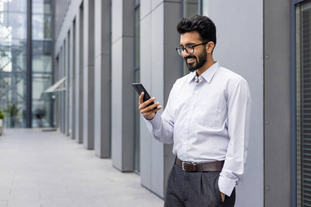 istock Confident businessman smiling and using smartphone outside modern office building 2148436573