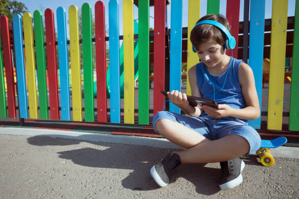 Two children, one using a tablet and one with a ball.  A concept for too much screen time for children.