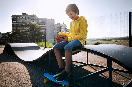 Happy smiling boy using smartphone in a skateboard park.